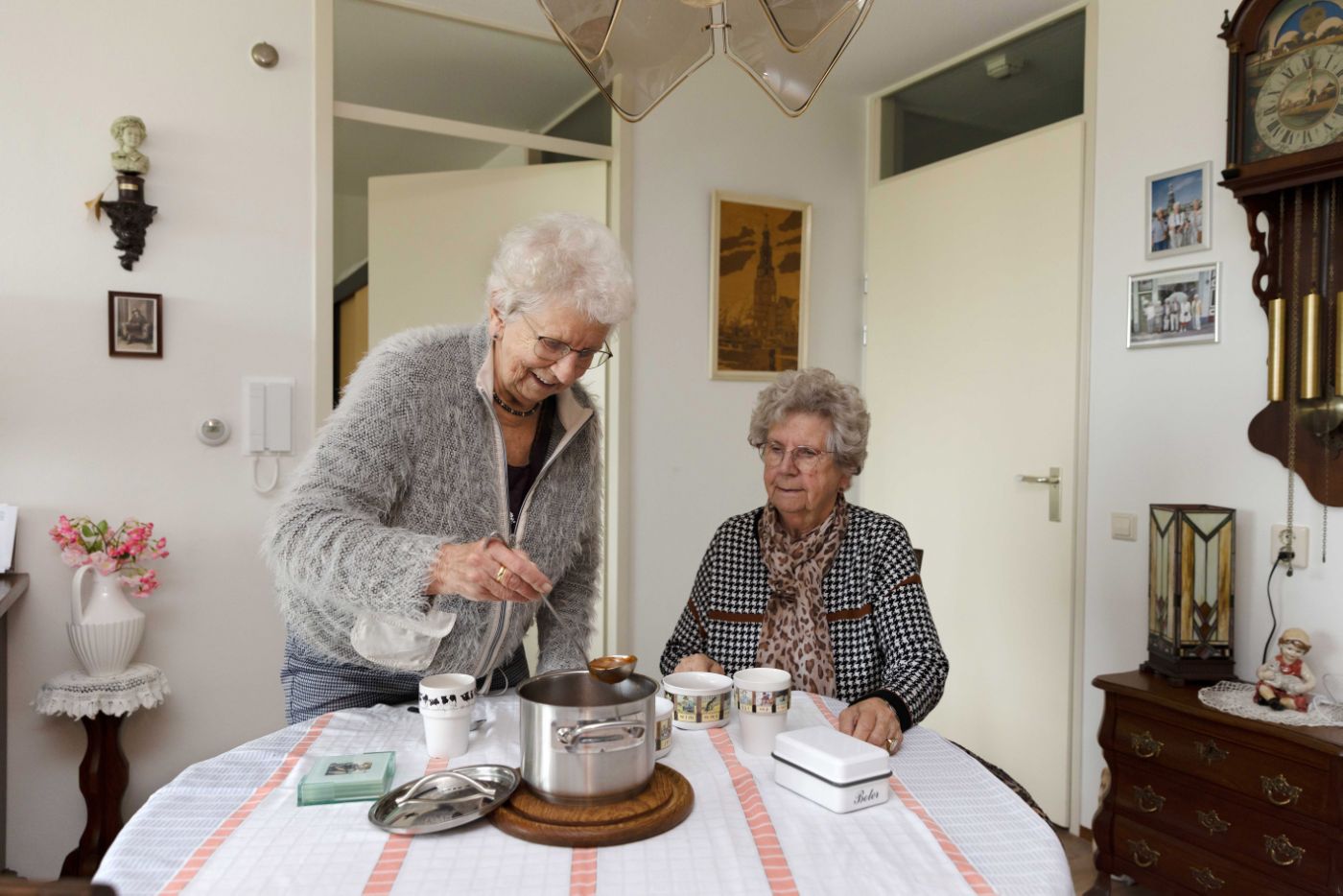 Cliënt en mantelzorger in keuken aan tafel eten soep opscheppen Mantelzorger schept soep op voor haar oude zus in de keuken van huis