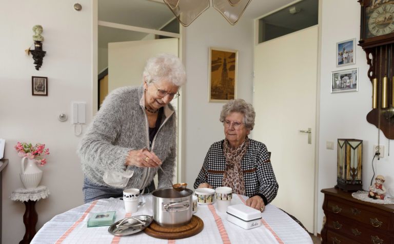 Cliënt en mantelzorger in keuken aan tafel eten soep opscheppen Mantelzorger schept soep op voor haar oude zus in de keuken van huis