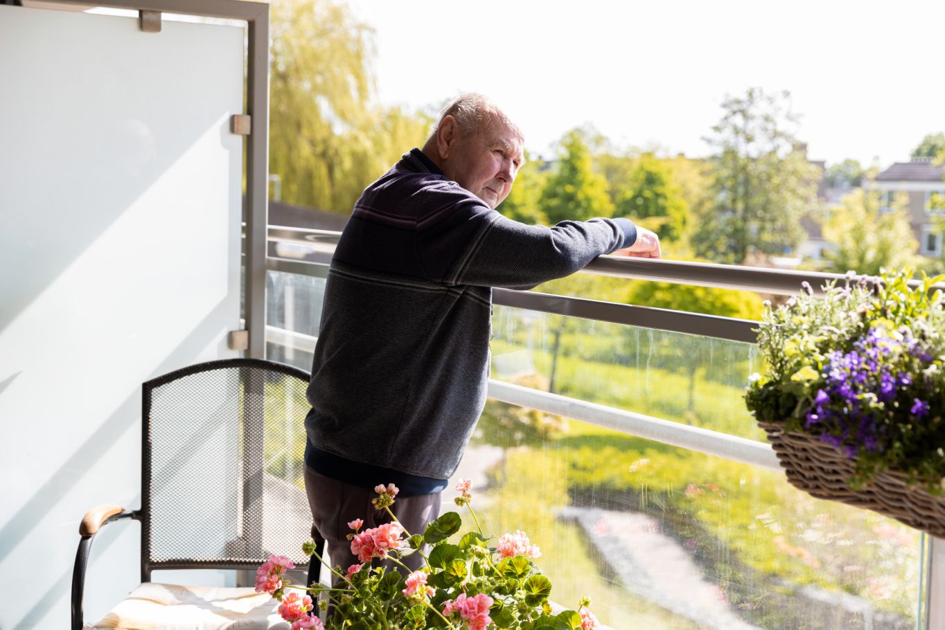 Client bewoner Riederborgh op balkon met bloemen en uitzicht op Ridderkerk Oude meneer staat op het balkon en kijkt naar beneden
