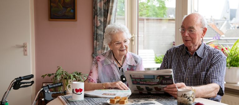 Client echtpaar koffie krant tafel thuis Oud echtpaar drinkt koffie aan tafel in huis en leest de krant met rollator en alarmeringsknop