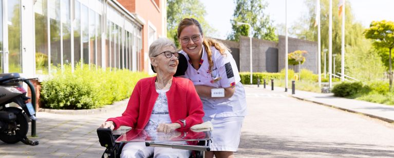 Client scootmobiel zorgmedewerker buiten vacature Riederborgh verpleeghuiszorg uniform Cliënt in scootmobiel rijdt buiten over straat met zorgmedewerker lachend erachter