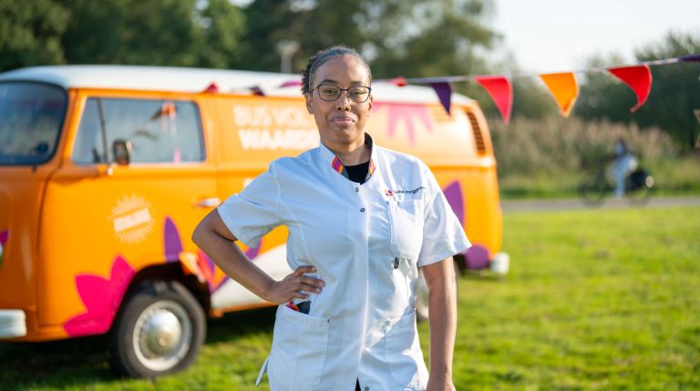Dania website vacature zorg bus vol waardering thuiszorg thuiszorg verpleeghuiszorg uniform Siloam Vrouw in uniform zorgmedewerker poseert glimlachend voor oranje vintage volkswagenbusje van Lelie zorggroep