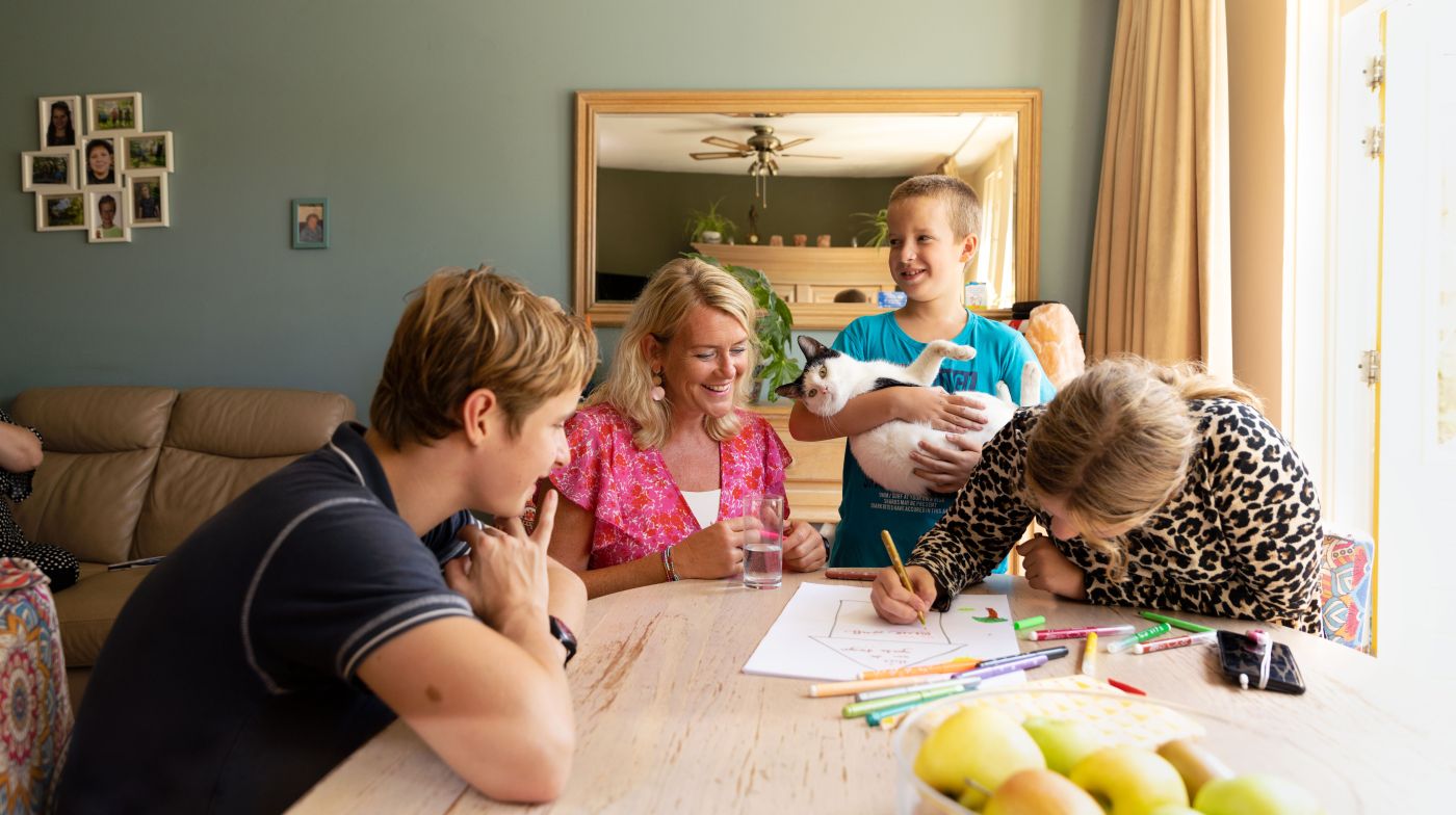 Familie en hulpverlener aan tafel tekenen Vrouwelijke hulpverlener zit aan tafel met een moeder en kinderen en tekent op papier