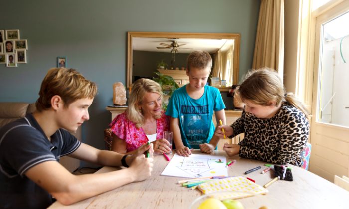 Gezin tekenen aan tafel met hulpverlener vacature hulpverlening Kinderen uit een gezin praten met hulpverlener en tekenen op papier