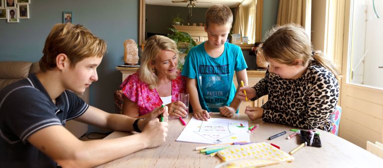 Gezin tekenen aan tafel met hulpverlener vacature hulpverlening Kinderen uit een gezin praten met hulpverlener en tekenen op papier