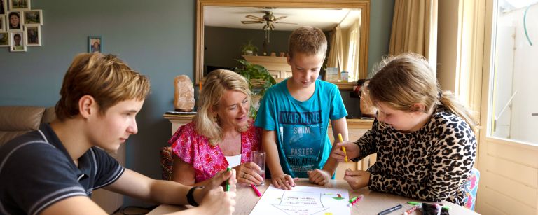 Gezin tekenen aan tafel met hulpverlener vacature hulpverlening Kinderen uit een gezin praten met hulpverlener en tekenen op papier