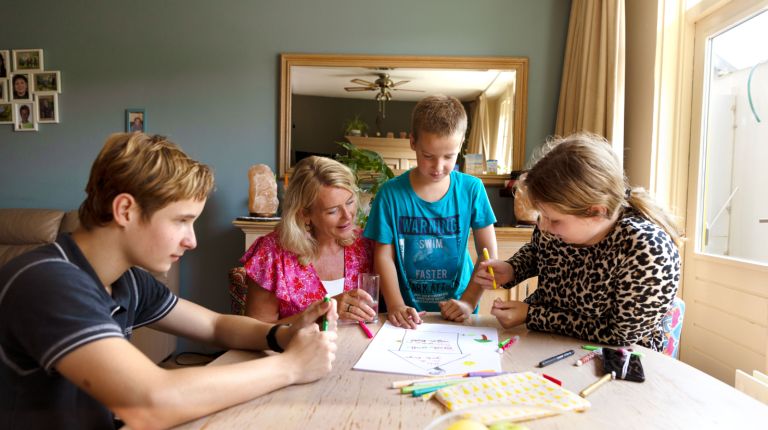 Gezin tekenen aan tafel met hulpverlener Vrouwelijke hulpverlener begeleidt drie kinderen aan tafel door tekeningen en gesprek.