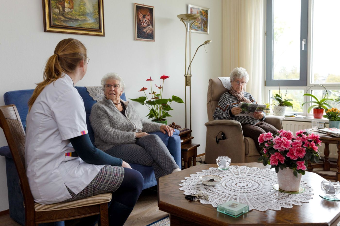 Huiskamer cliënt met mantelzorger en zorgmedewerker Zorgmedewerker zit in de huiskamer met twee oude vrouwen