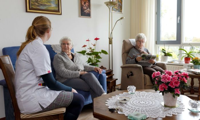 Huiskamer cliënt met mantelzorger en zorgmedewerker Zorgmedewerker zit in de huiskamer met twee oude vrouwen