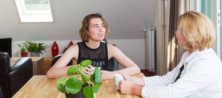 Hulpverlener client jongere gesprek huis Jongvolwassen vrouw en vrouwelijke hulpverlener zitten aan tafel samen in gesprek