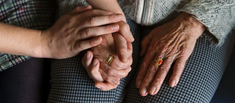 Jonge en oude handen op elkaar Jonge handen houden oude handen met ring vast op schoot