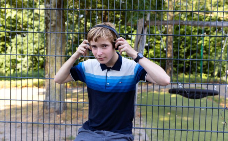 Jongen luistert muziek met koptelefoon Een jonge tiener luistert buiten naar muziek met koptelefoon