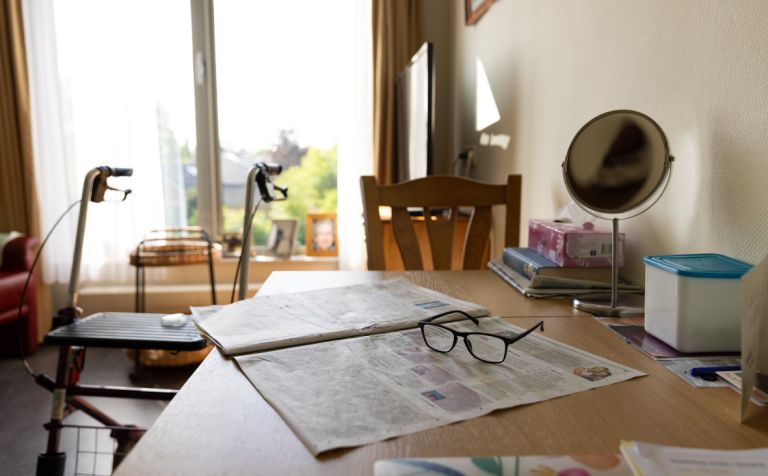 Krant rollator bril kamer bewoner verpleeghuis Krant en bril op tafel in een kamer van een bewoner in het verpleeghuis met een rollater op de achtergrond