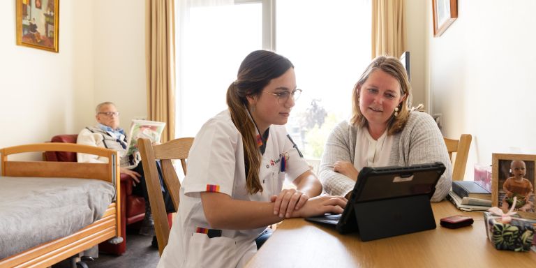 Mantelzorger bewoner zorgmedewerker Riederborgh tablet Vrouwelijke mantelzorger bespreekt samen met een zorgmedewerker bij een tablet met een client op de achtergrond