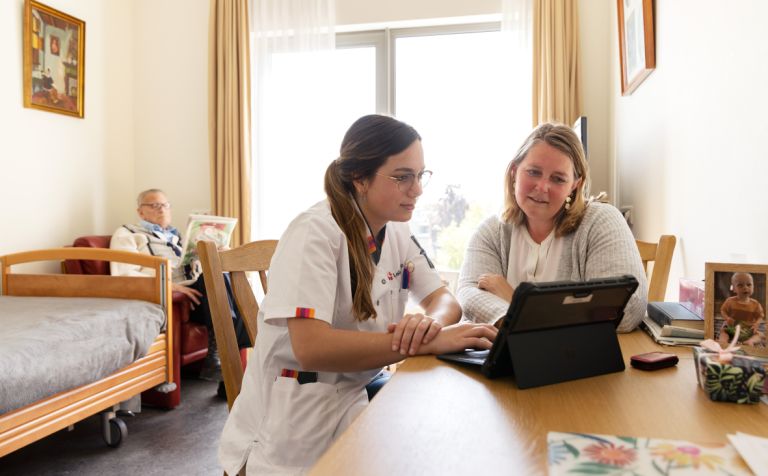 Mantelzorger bewoner zorgmedewerker Riederborgh tablet Vrouwelijke mantelzorger bespreekt samen met een zorgmedewerker bij een tablet met een client op de achtergrond