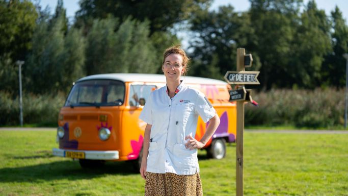 Vrouw van christelijke zorgorganisatie Lelie Zorggroep in Rotterdam zorg thuiszorg verpleeghuiszorg bus vol waardering vacature uniform Vrouwelijke zorgmedewerker poseert glimlachend voor oranje vintage volkswagenbusje van Lelie zorggroep