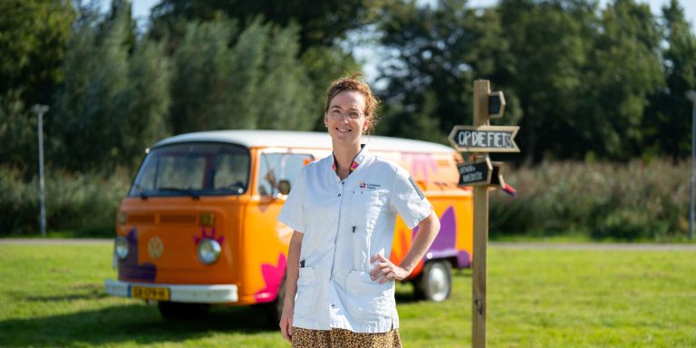 Vrouw van christelijke zorgorganisatie Lelie Zorggroep in Rotterdam zorg thuiszorg verpleeghuiszorg bus vol waardering vacature uniform Vrouwelijke zorgmedewerker poseert glimlachend voor oranje vintage volkswagenbusje van Lelie zorggroep