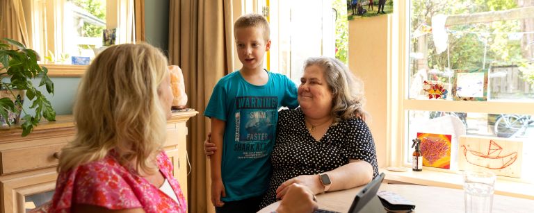 Moeder kind en hulpverlener aan tafel Moeder, vrouwelijke hulpverlener en jongen zitten aan de keukentafel in huis