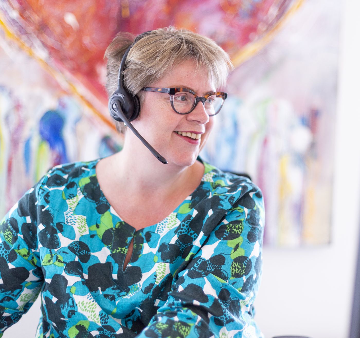Receptioniste lachend achter receptie van Lelie zorggroep Receptioniste zit lachend achter computer met headset bij receptie van Lelie zorggroep