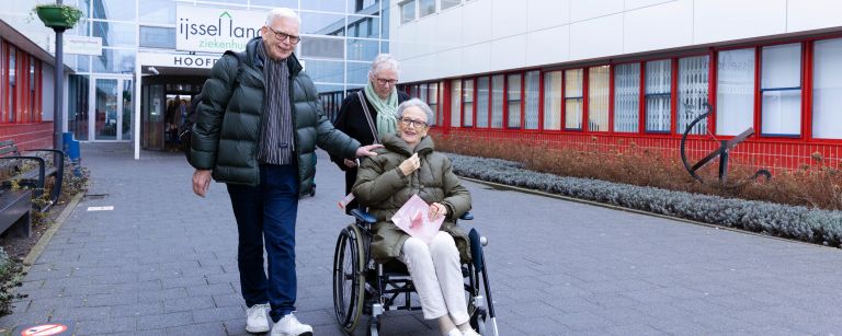 Revalidatie cliënt in rolstoel voor hoofdingang IJsselland Client zit in een rolstoel met familieleden om haar heen voor het IJsselland Ziekenhuis