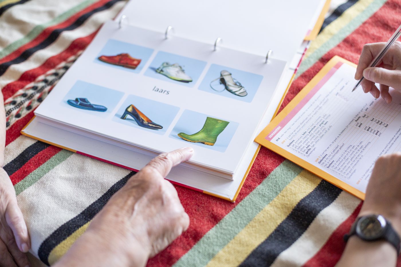 Logopedie Lelie zorggroep in Rotterdam, Ridderkerk en Krimpen a/d IJssel Oude hand wijst laars aan in boekje met zes plaatjes waarbij het woord 'laars' in het midden staat.
