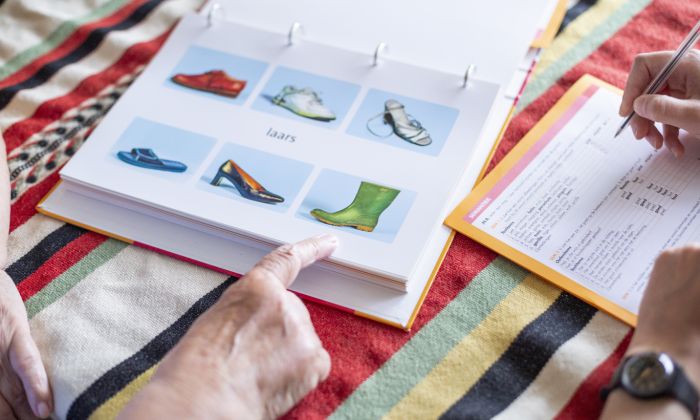 Logopedie Lelie zorggroep in Rotterdam, Ridderkerk en Krimpen a/d IJssel Oude hand wijst laars aan in boekje met zes plaatjes waarbij het woord 'laars' in het midden staat.