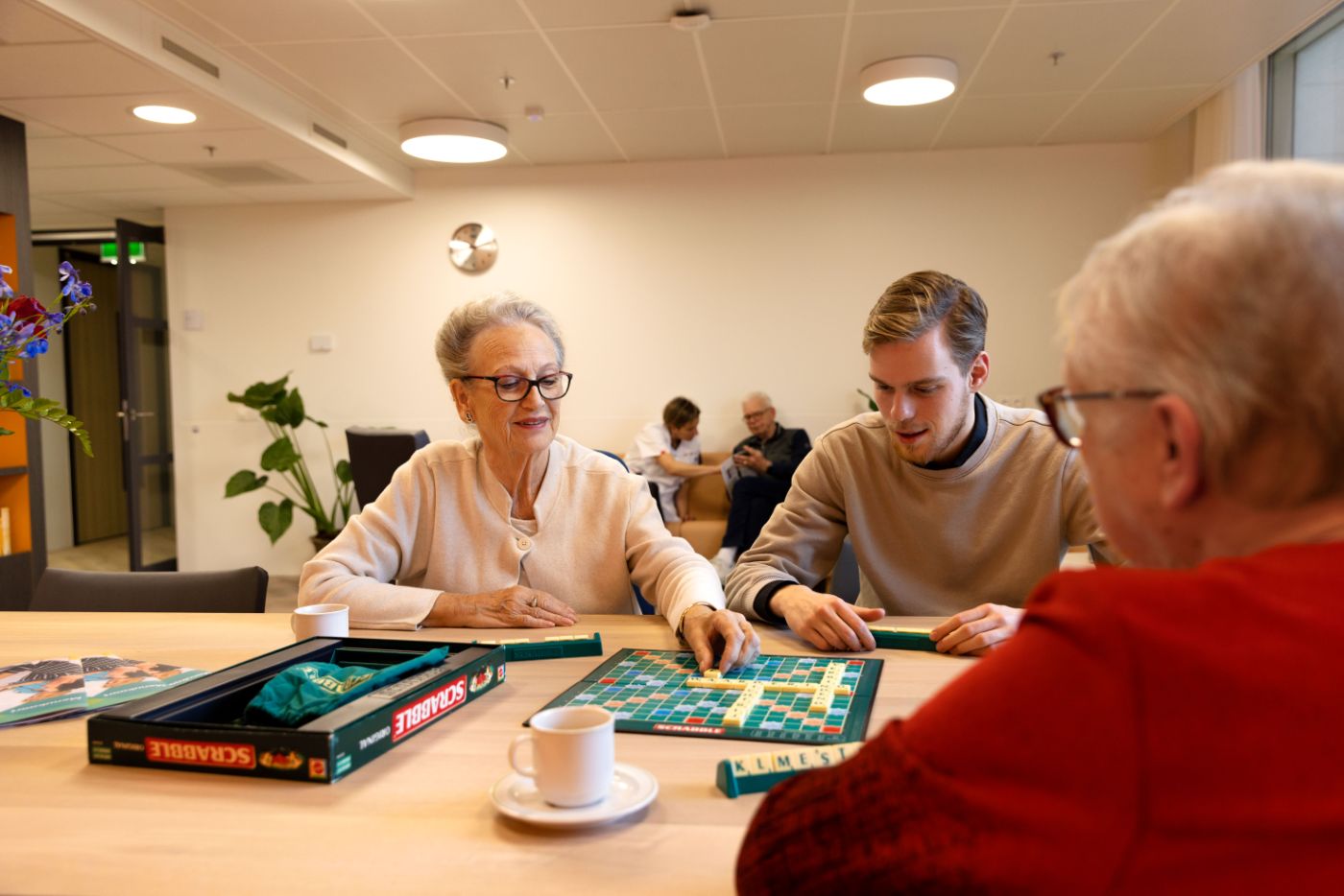 Spelletje scrabble aan tafel bij dagbesteding christelijke zorgorganisatie Lelie zorggroep IJsselland Schenkel vacature welzijn vrijwilliger Jonge man speelt een spelletje scrabble met oude mevrouw