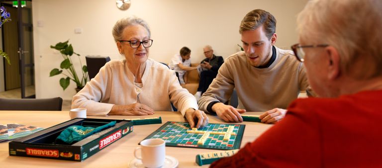 Spelletje scrabble aan tafel Jonge man speelt een spelletje scrabble met oude mevrouw