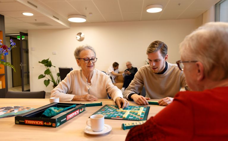 Spelletje scrabble aan tafel Jonge man speelt een spelletje scrabble met oude mevrouw