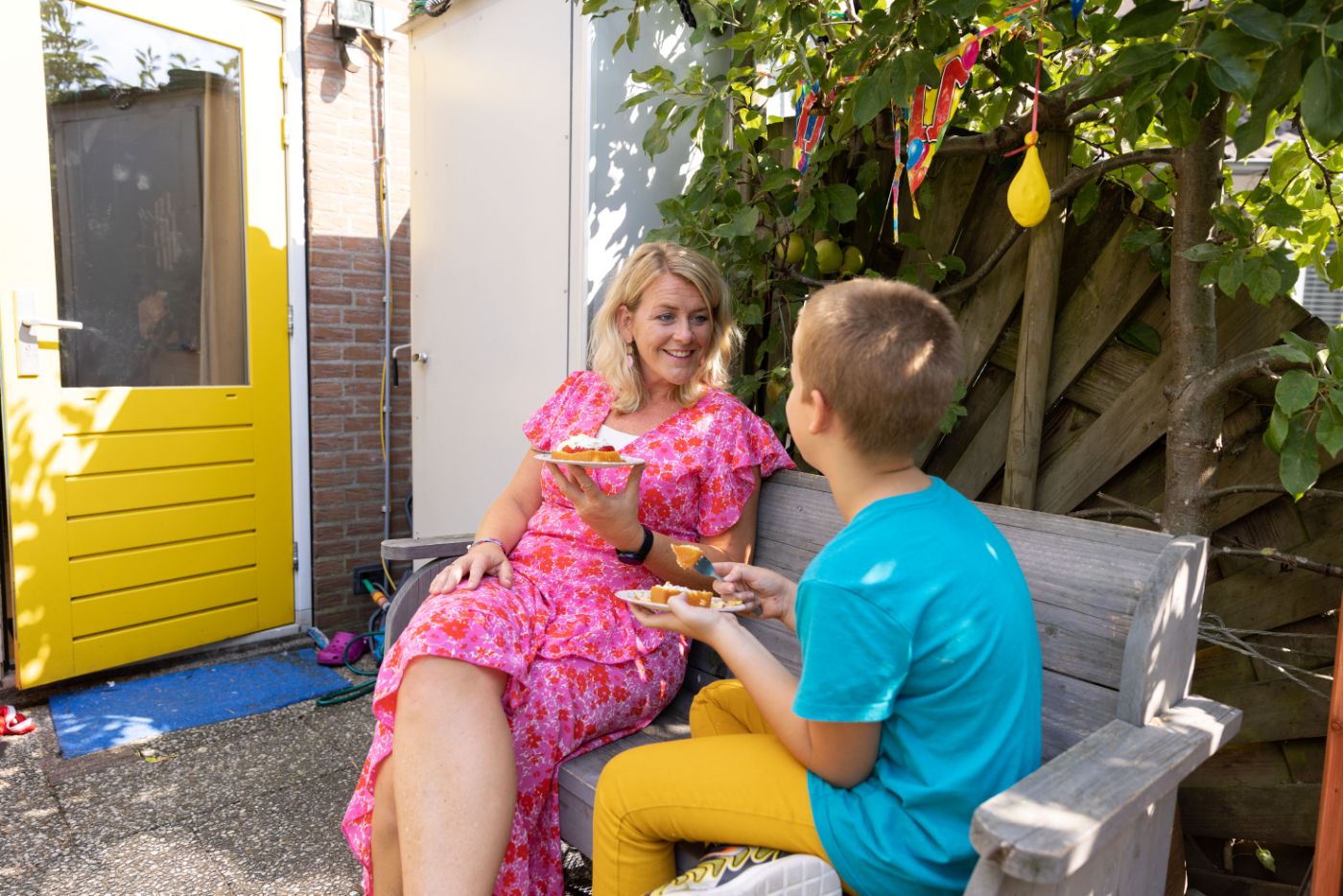 Taart op bank ik tuin kind en hulpverlener vacature hulpverlening Hulpverlener en kind zitten buiten op een bankje een taartje te eten