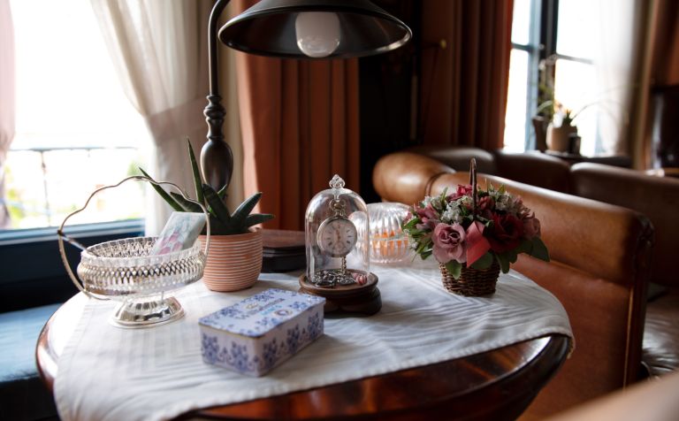 Tafel huiskamer client thuiszorg Ronde tafel met tafelkleed en antiek klokje, planten, glazen bakjes en doos