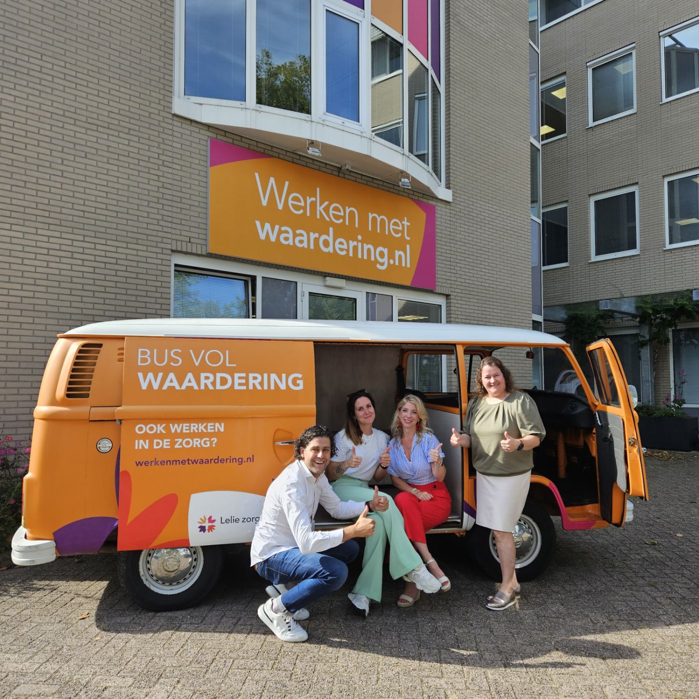 Vier medewerkers van de afdeling werving zitten met opgestoken duimen voor de oranje volkswagen bus vol waardering Vier medewerkers van de afdeling werving zitten met opgestoken duimen voor de oranje volkswagen bus vol waardering