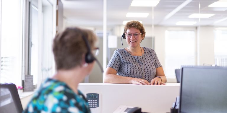 Twee receptionistes van Lelie zorggroep bij receptie service vacature Twee vrouwelijke receptionistes van de christelijke zorgorganisatie Lelie zorggroep staan bij receptie