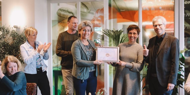 Uitreiking bronzen keurmerk Milieu Platform Zorgsector aan locatie Oranjehof Groepsfoto waarbij de locatiemanager van verpleeghuis Oranjehof het bronzen keurmerk krijgt van de directeur van Milieu Platform Zorgsector