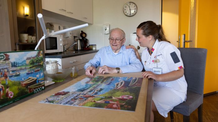 Zorgmedewerker en client woonkamer keuken puzzel vacature Riederborgh verpleeghuiszorg Zorgmedewerker en cliënt van Riederborgh zitten in de woonkamer een puzzel te maken