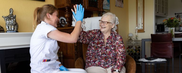Zorgverlener en cliënt in woonkamer high five vacature thuiszorg Zorgverlener en cliënt zijn blij met het resultaat van de verpleging en verzorging