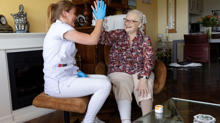 Zorgverlener en cliënt in woonkamer high five Vrouwelijke zorgverlener en oude dame geven elkaar in de woonkamer van een huis een high five