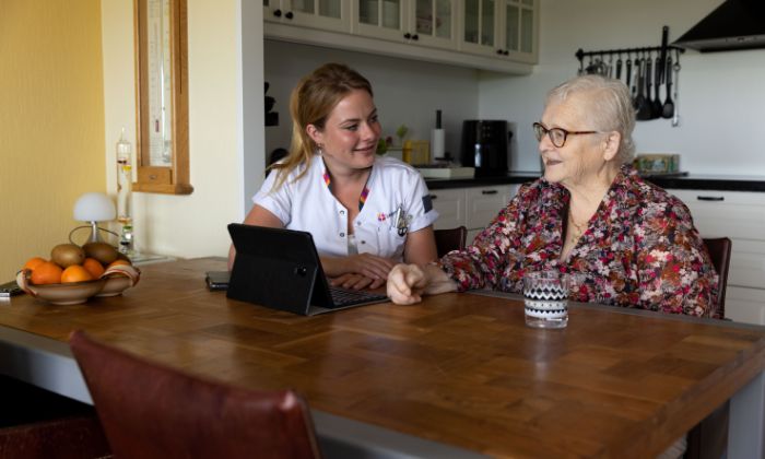Zorgverlener en cliënt met tablet aan tafel vacature thuiszorg Zorgverlener en cliënt met tablet aan tafel vacature thuiszorg