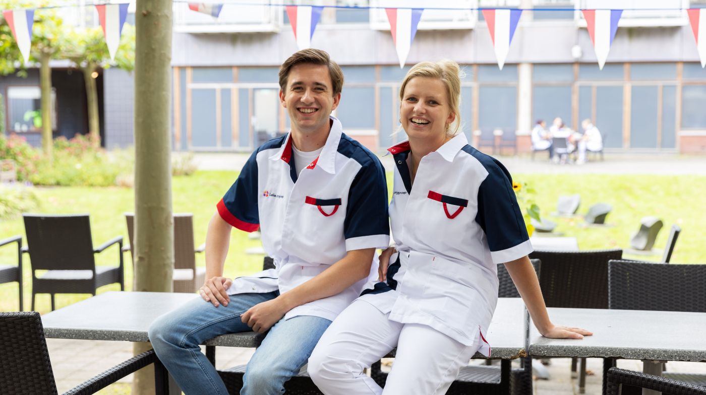 Zorgverleners collegas christelijk verpleeghuis Pniël portret buiten in de tuin Een jonge vrouwelijke en mannelijke zorgverlener zitten geposeerd buiten op de tafel